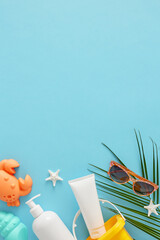 Baby summer skincare concept. Top view vertical flat lay of cosmetic bottles, beach toys, sunglasses, starfish and palm leaf on light blue background with space for text or advert