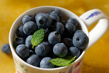 Close up of blueberries in a mug on yellow background.