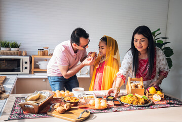 an Indian family standing in the kitchen They are eating and preparing many foods on the table, to family and Indian food concept.