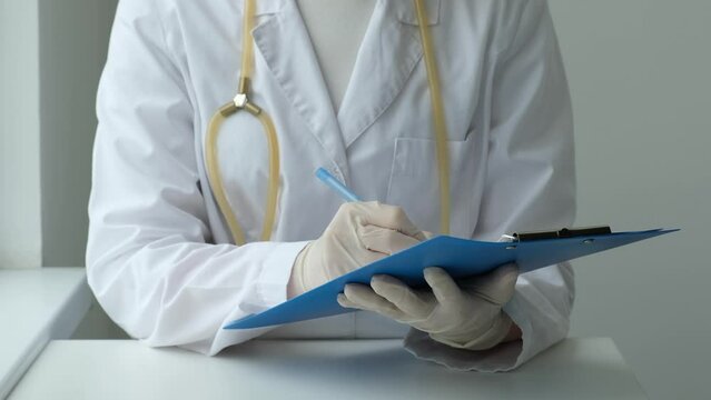 Female doctor filling up medical form at clipboard in clinic. Physician with stethoscope holding notebook in hand. Health care, medicine concept