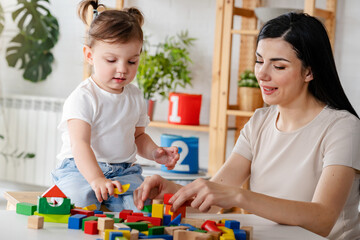 Young woman and small child playing with colorful wooden building blocks