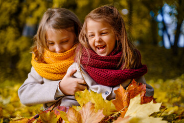 Beautiful little girls in bright yellow red orange autumn warm knitted scarf snood with head wreath of maple leaves,foliage walking in forest. Fun playing in park. Outdoor family activity in nature