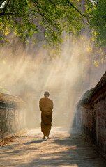 Vertical image of Back of Asian monk walk on the way along with old wall of ancient palace or building with linne beam light.