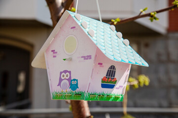 A birdhouse in the form of a white house on the background of city houses. Improvement of the city...