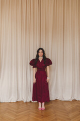 Girl in the cherry dress standing near blind. Women's health, sexuality. Portrait of a beautiful young woman in cherry dress with belt and puff sleeves. Sexy brunette woman look sensual.
