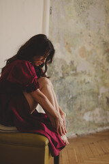 Girl in the cherry dress sitting on green chair. Women's health, sexuality. Portrait of a beautiful young woman in cherry dress with belt and puff sleeves. Sexy brunette woman look sensual.