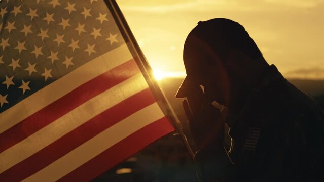 Silhouette of American soldier praying for memorial day against the flag outdoor
