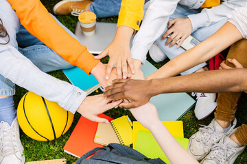 Diverse student people stacking hands together sitting outdoors at college campus. Youth community concept with young group of millennial students joining hands together showing unity and oneness.