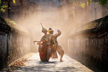 Fototapeta premium Beautiful Asian woman wear Thai traditional dress action of dancing together with Thai classic masked from the Ramakien character as black monkey with ancient wall and buildin in mist background.