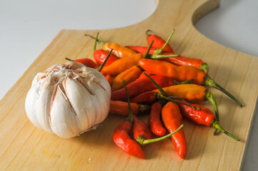 Several red and yellow chilies and a garlic bulb on a wooden board isolated on a white background