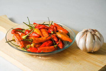 Some red and yellow chilies in a small plate and a garlic bulb on a wooden cutting board isolated on a white background