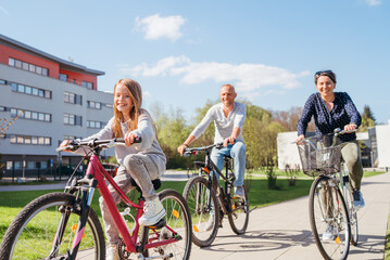 Smiling long-haired little girl with father and mother during summer city outdoor bicycle riding....