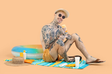 Tattooed man with sunscreen cream and beach accessories on beige background