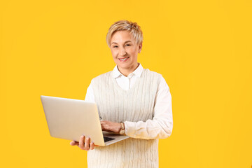 Mature female programmer working with laptop on yellow background