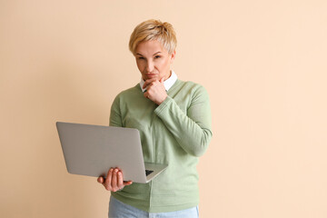 Thoughtful mature female programmer with laptop on beige background