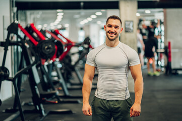 Fototapeta na wymiar Portrait of a happy sportsman with big muscles standing in a gym and smiling at the camera.