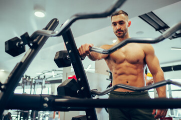 Fototapeta na wymiar A young focused shirtless muscular sportsman is choosing exercise equipment at the gym.