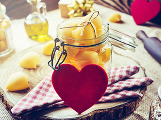 Lumaconi pasta in a glass jar on a wooden background in the morning sun. Red hearts and a gift. Valentine's Day. selective focus