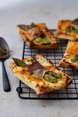 Puff pastry tart with green asparagus and bacon. Asparagus pie with cheese and bacon on a light background