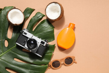 Palm leaf with coconut, photo camera, sunglasses and sunscreen cream on beige background