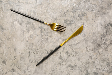 Golden fork and knife with black handles on grey background
