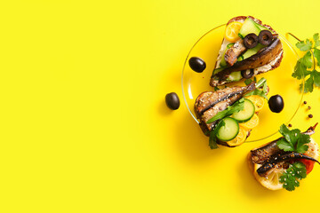 Plate of tasty sandwiches with canned smoked sprats on yellow background