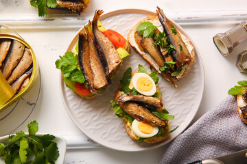 Plate of tasty sandwiches with canned smoked sprats on white wooden background