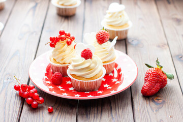 Vanilla cupcakes decorated with fresh strawberry, raspberry and red currant on rustic wooden background