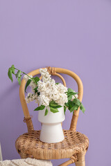 Vase with lilac flowers on chair near color wall