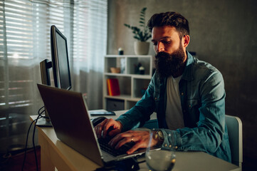 A data entry scientist typing on his laptop while sitting at his modern home office.