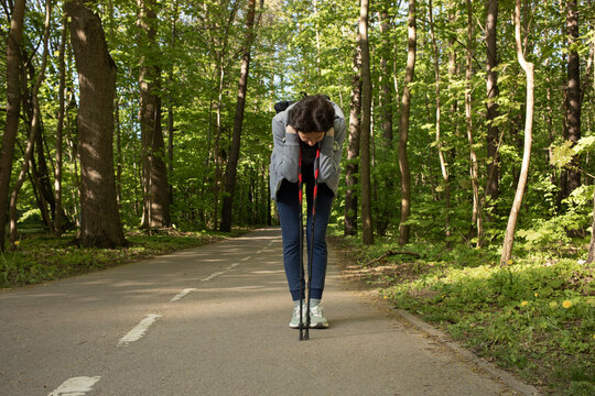 Woman bends over leaning walking poles feeling pain, not well while doing sport, jogging, Nordic walk in Park.Hard breathing, Dizziness. Sickness during incorrect workout. Horizontal Plane, Copy Space