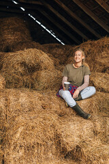 Naklejka na ściany i meble A beautiful Caucasian woman sits in a pile of hay