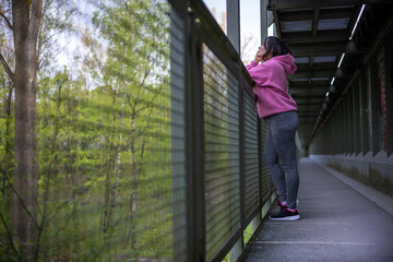 woman running outside,crossing bridge,exercising,tie the sneakers laces.young girl,female with weight problem loss,sport fitness diet,slim fit concept.spring green nature,resting woman.pink hoodie.