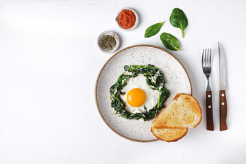 Fried eggs with fresh spinach and creamcheese on a plate om white background, top view, copy space