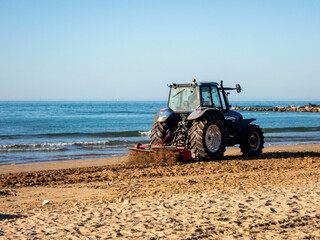 Aratura della spiaggia con un trattore in una giornata di sole - obrazy, fototapety, plakaty