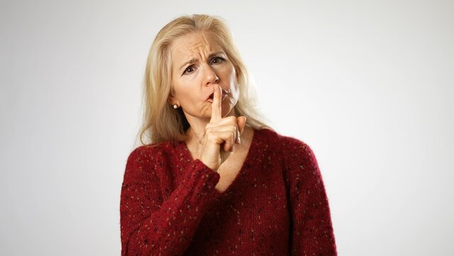 Portrait of angry upset frustrated angry senior mature woman saying shh, quiet, with blond hair on green screen background.