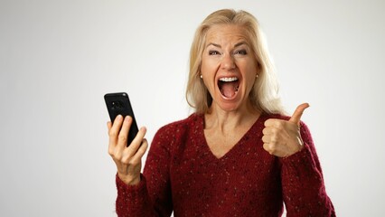 Happy middle aged woman holding smartphone, using mobile applications pointing to phone isolated on white background.