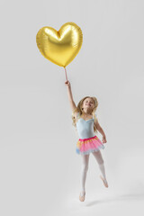 Studio portrait of adorable little girl holding large golden heart shaped balloon