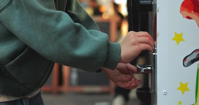 Five year old child insert coin into game or vending machine and rotate knob. Closeup shot of preschool kid hands use toy machine.