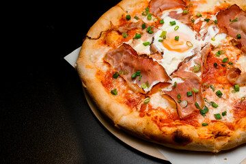 freshly baked pizza with bacon, egg, cheese and onion on wooden board on the table