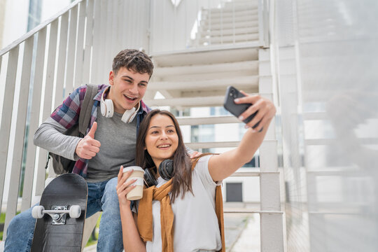 Two teenagers sitting on stairs holding mobile phone making selfies or a video call