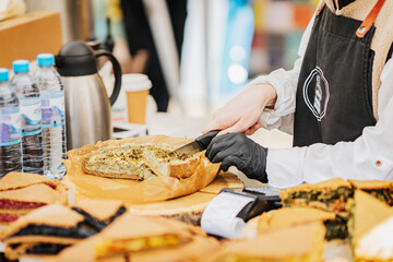 Girl Chef cook in apron and gloves cuts freshly baked pie in market. Street food