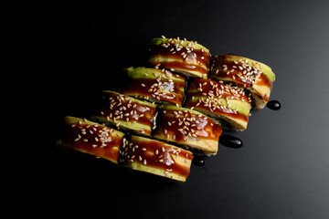 top view of tasty green dragon sushi rolls with salmon, avocado, cucumber and green caviar poured with teriyaki sauce.
