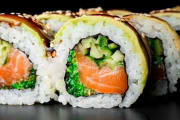 Asian sushi rolls with salmon, avocado, cucumber and green caviar poured with teriyaki sause.