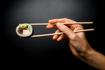 Man's hand holds tasty sushi roll with smoked eel, avocado, cucumber and cheese with chopsticks