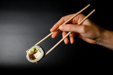Man's hand gently holds tasty asian sushi roll with smoked eel, avocado, cucumber and cheese using chopsticks