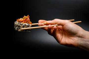 side view of one piece of roll with caramelized onion, raw fish, sesame and rice in hand