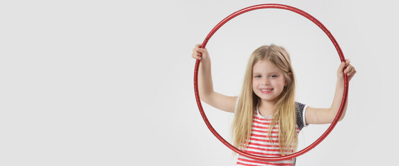 Studio portrait of beautiful cheerful little girl playing with red hula hoop
