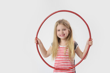 Studio portrait of beautiful cheerful little girl playing with red hula hoop © triocean