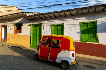 little motorbike, little red three-wheeled car next to a colorful house in latin america